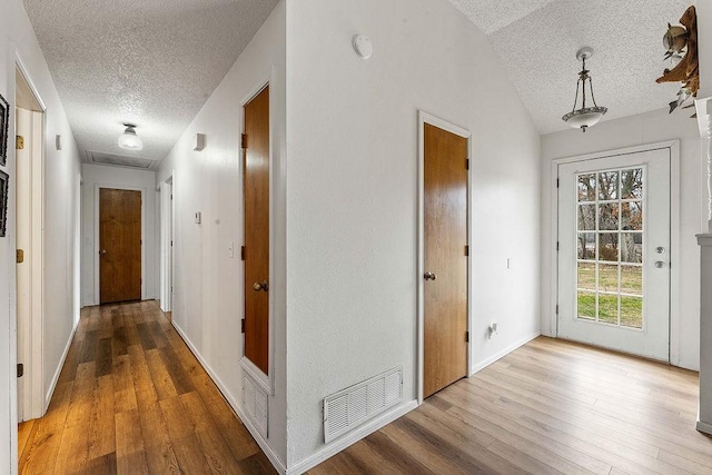 hallway with visible vents, lofted ceiling, a textured ceiling, and wood finished floors