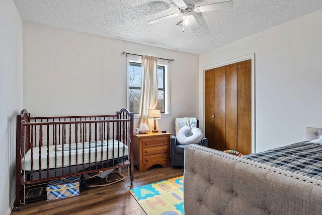 bedroom featuring a ceiling fan, wood finished floors, a crib, and a textured ceiling