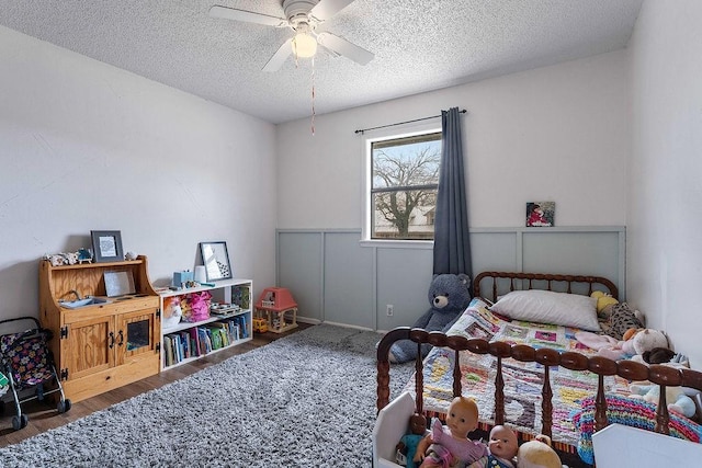 bedroom with wainscoting, a textured ceiling, ceiling fan, and wood finished floors