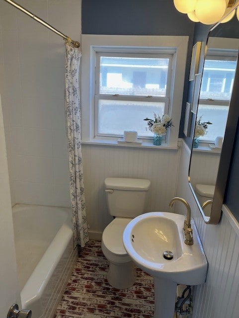 full bath featuring a sink, a wainscoted wall, shower / bathtub combination with curtain, and toilet