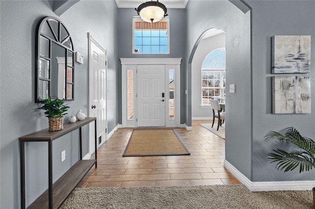 entryway featuring visible vents, baseboards, wood tiled floor, arched walkways, and ornamental molding