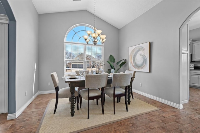 dining space featuring baseboards, a chandelier, lofted ceiling, wood finished floors, and arched walkways