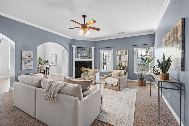 carpeted living room with baseboards, ornamental molding, a warm lit fireplace, arched walkways, and a textured ceiling