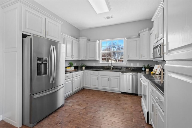 kitchen with visible vents, a sink, white cabinets, appliances with stainless steel finishes, and dark countertops