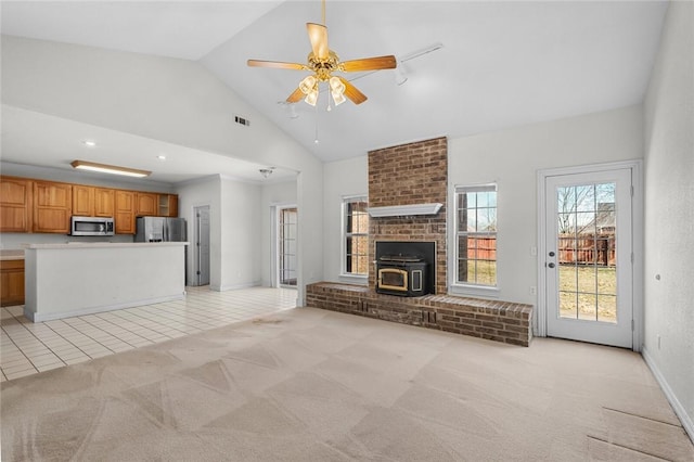 unfurnished living room featuring light tile patterned floors, visible vents, high vaulted ceiling, a wood stove, and light carpet