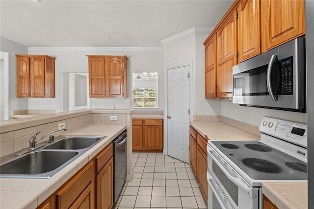 kitchen with tile countertops, appliances with stainless steel finishes, crown molding, and a sink