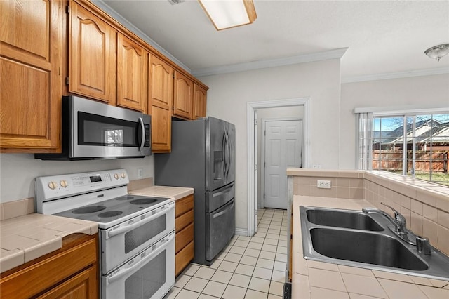 kitchen with a sink, appliances with stainless steel finishes, tile counters, and ornamental molding