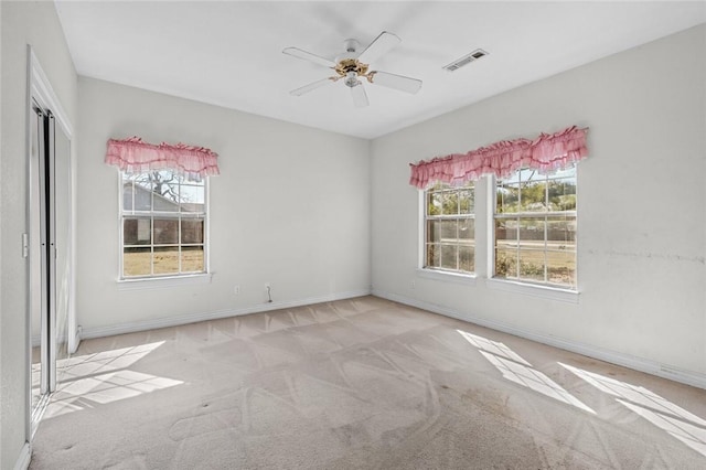 carpeted spare room featuring baseboards, visible vents, and ceiling fan