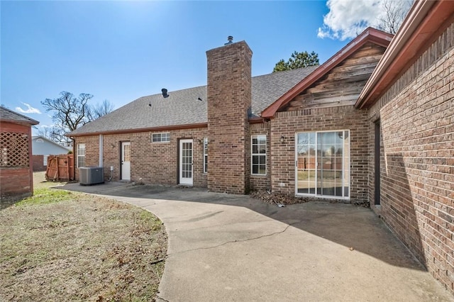 back of property with brick siding, a shingled roof, central AC unit, a chimney, and a patio area