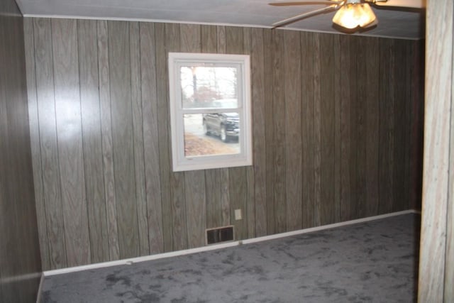 carpeted spare room featuring visible vents, baseboards, wooden walls, and ceiling fan