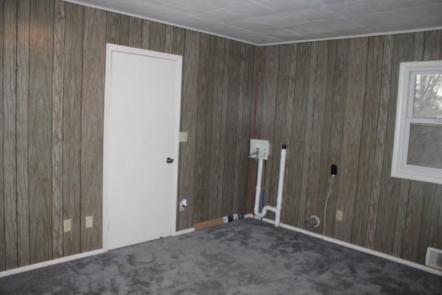 carpeted empty room featuring wood walls