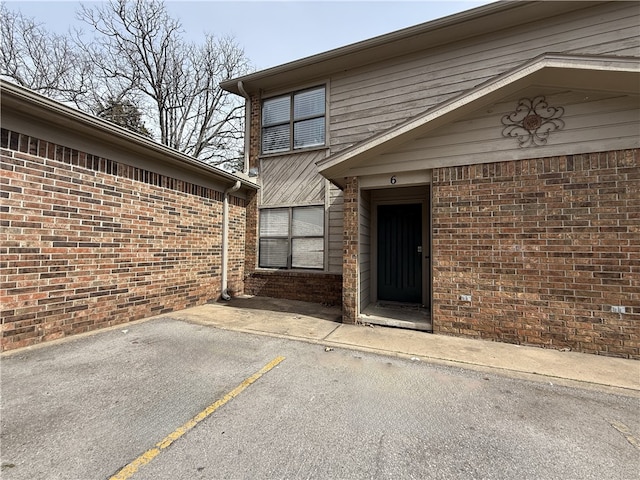 entrance to property with a patio, brick siding, and uncovered parking