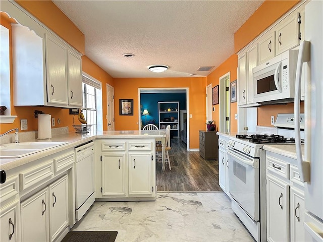 kitchen with visible vents, light countertops, a peninsula, white appliances, and a sink