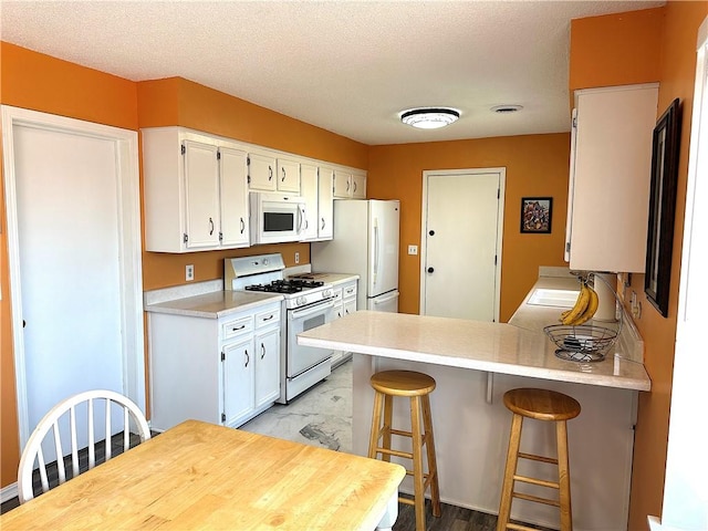 kitchen with a breakfast bar, marble finish floor, white appliances, white cabinets, and light countertops