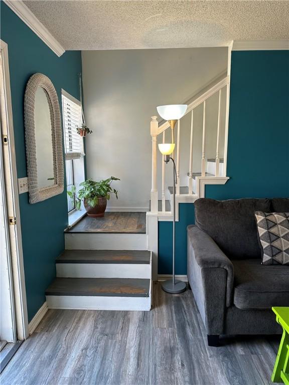 stairway featuring baseboards, a textured ceiling, wood finished floors, and ornamental molding