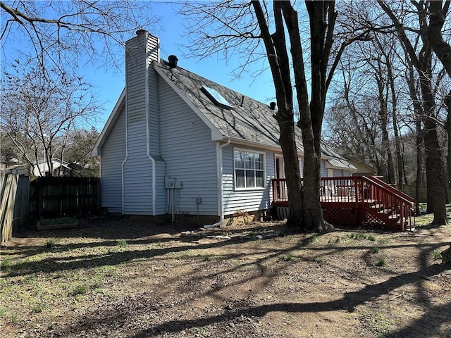 view of home's exterior with a shingled roof, a deck, a chimney, and fence