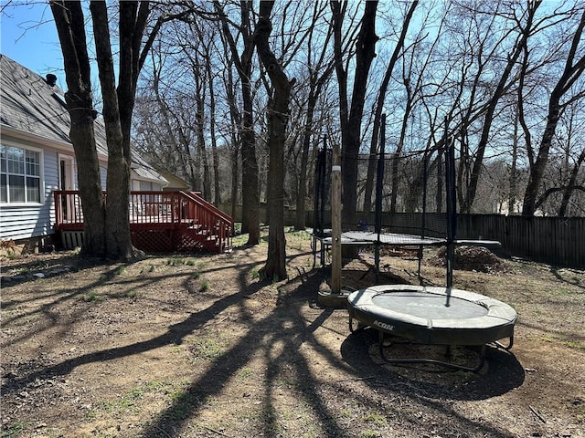 view of yard with a deck, a trampoline, and fence