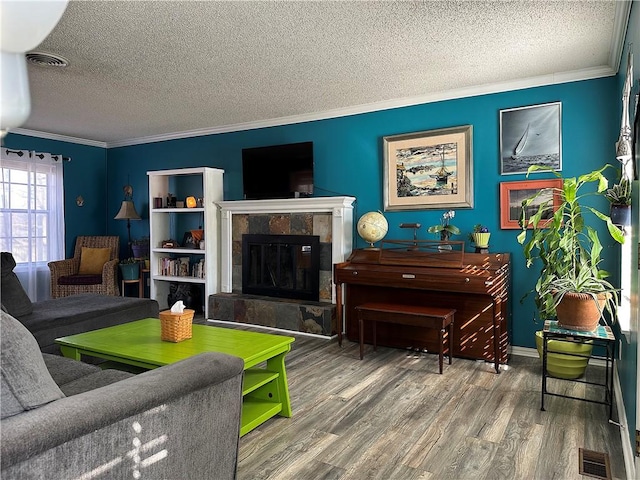 living room with visible vents, wood finished floors, crown molding, and a tiled fireplace