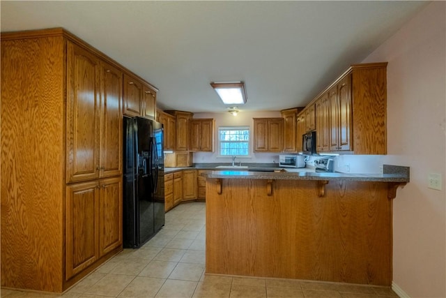 kitchen with black appliances, a breakfast bar, a sink, a peninsula, and brown cabinetry