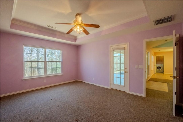 carpeted empty room with a tray ceiling, washer / clothes dryer, crown molding, and visible vents