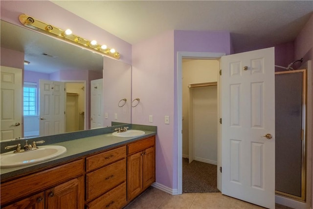 bathroom featuring tile patterned floors, a stall shower, double vanity, and a sink