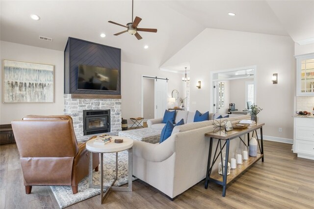 living room with visible vents, wood finished floors, a barn door, a stone fireplace, and vaulted ceiling