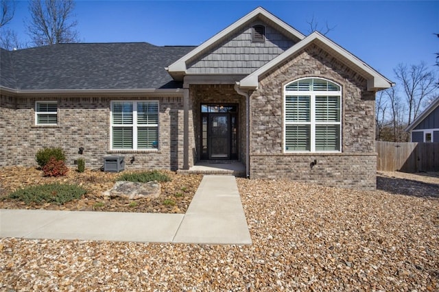 view of front of property with brick siding, roof with shingles, and fence