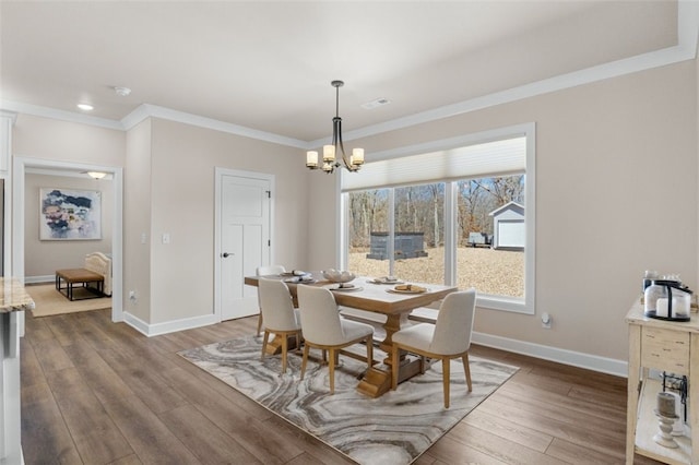 dining space featuring baseboards, an inviting chandelier, wood finished floors, and crown molding