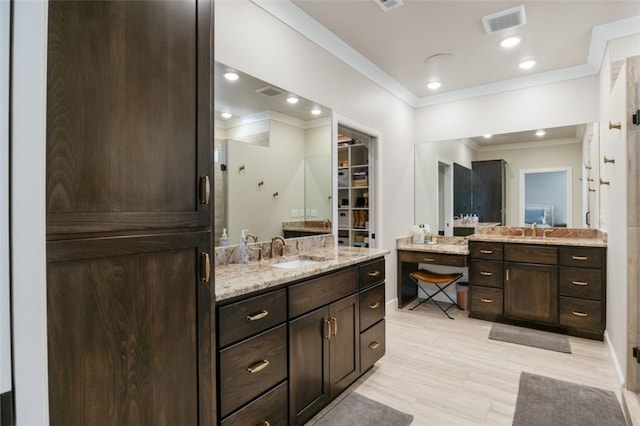 full bath with a sink, two vanities, and ornamental molding