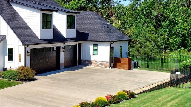 view of front facade with board and batten siding, concrete driveway, roof with shingles, and fence