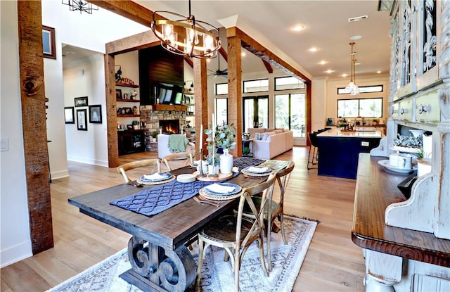 dining space with ceiling fan with notable chandelier, visible vents, a fireplace, and light wood-style floors