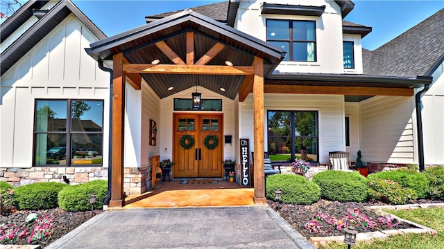 property entrance with covered porch, board and batten siding, stone siding, and a shingled roof