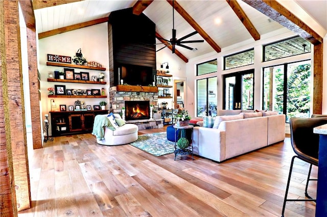 living area with beamed ceiling, high vaulted ceiling, a ceiling fan, wood finished floors, and a stone fireplace