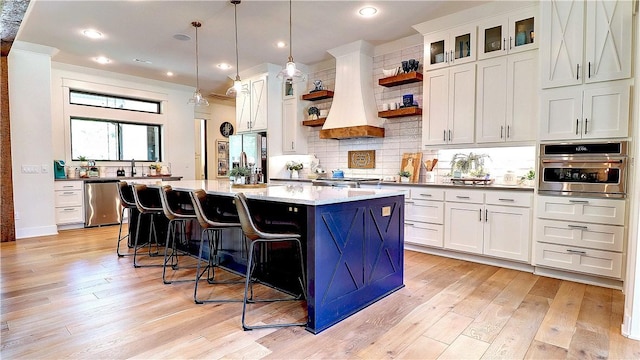 kitchen with premium range hood, light wood-type flooring, open shelves, tasteful backsplash, and stainless steel appliances