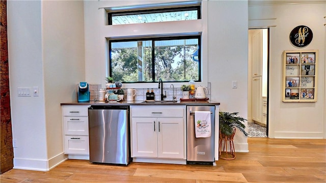 bar featuring a sink, baseboards, dishwasher, and light wood finished floors