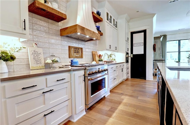 kitchen with island exhaust hood, open shelves, tasteful backsplash, stainless steel stove, and light wood finished floors