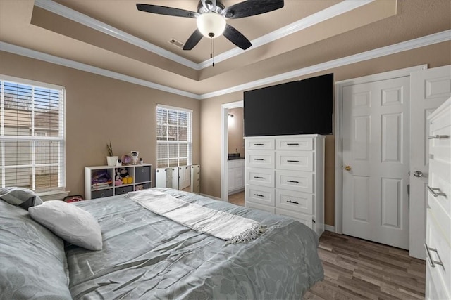 bedroom with a raised ceiling, wood finished floors, visible vents, and ornamental molding