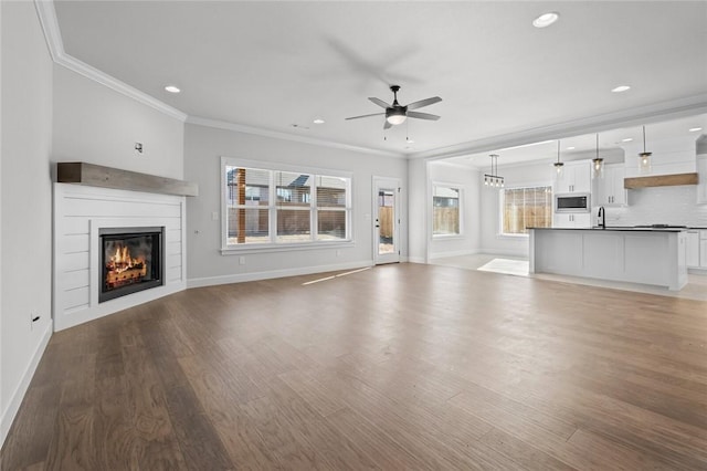 unfurnished living room with a ceiling fan, wood finished floors, ornamental molding, a sink, and a glass covered fireplace