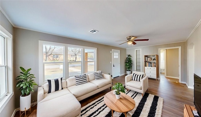 living area with visible vents, crown molding, baseboards, wood finished floors, and arched walkways