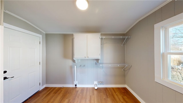 clothes washing area with cabinet space, crown molding, a healthy amount of sunlight, and wood finished floors