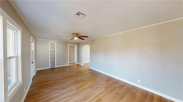 unfurnished room with arched walkways, visible vents, crown molding, and light wood-type flooring