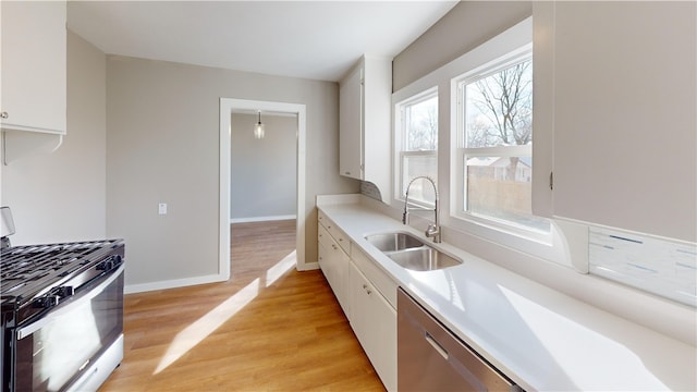 kitchen with a sink, stainless steel appliances, light countertops, light wood-style floors, and white cabinetry