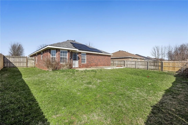 back of house featuring a lawn, solar panels, a fenced backyard, and brick siding