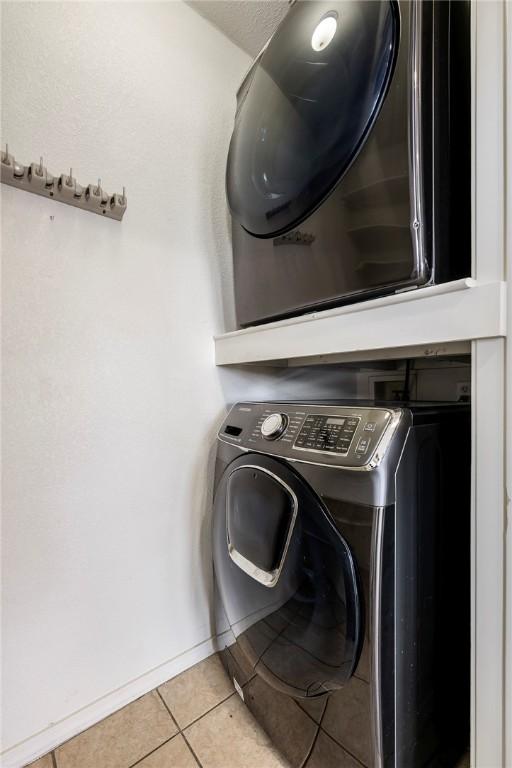 clothes washing area with light tile patterned floors, baseboards, laundry area, and stacked washing maching and dryer