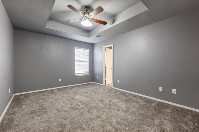 empty room with a raised ceiling, carpet flooring, baseboards, and visible vents