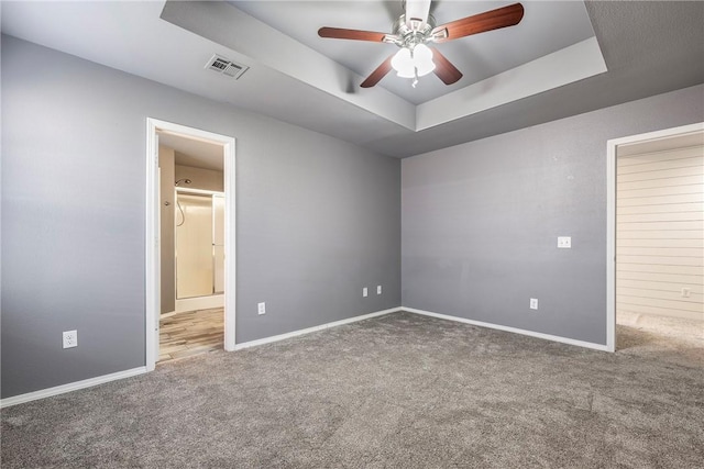 unfurnished bedroom featuring visible vents, ensuite bath, baseboards, carpet, and a raised ceiling