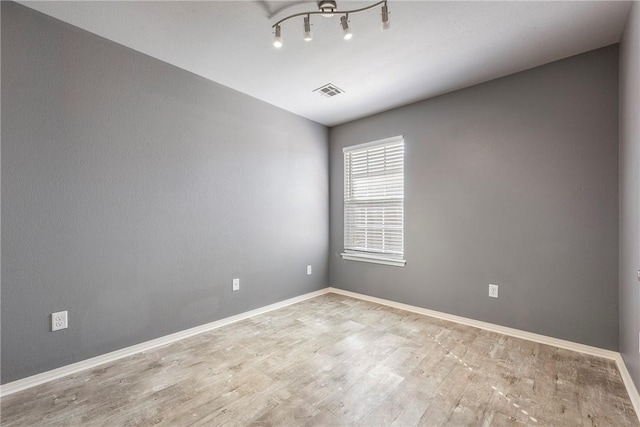 spare room featuring wood finished floors, visible vents, and baseboards