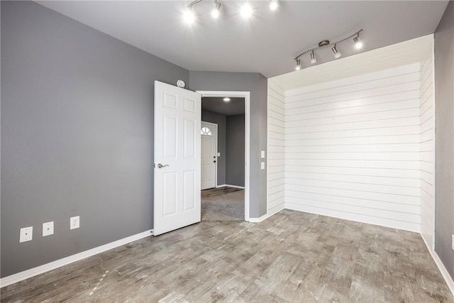 empty room featuring rail lighting, wood finished floors, and baseboards