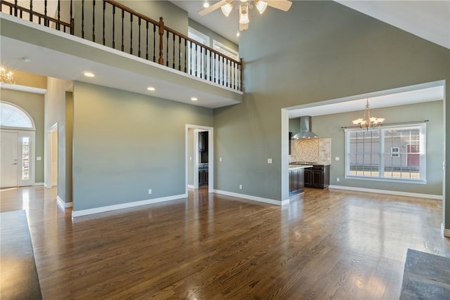 unfurnished living room with ceiling fan with notable chandelier, dark wood-type flooring, baseboards, and a towering ceiling