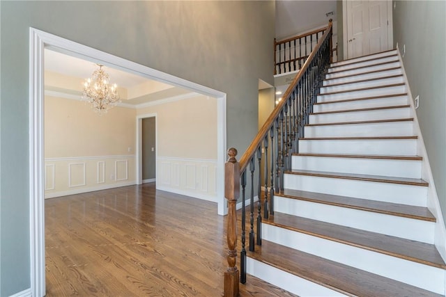 stairs featuring wood finished floors, a wainscoted wall, a chandelier, and ornamental molding